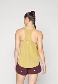 Camiseta atlética amarilla con diseño de espalda nadadora y dobladillo recto, combinada con pantalones cortos burdeos que presentan detalles de botones blancos.