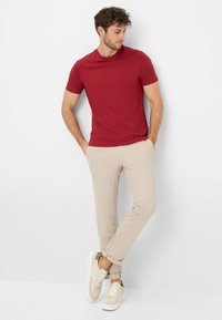 Rotes Kurzarm-T-Shirt mit Rundhalsausschnitt; kombiniert mit hellbeigen Chinos und beigen Sneakers mit strukturierten Details. Leger-Outfit vor weißem Hintergrund präsentiert.
