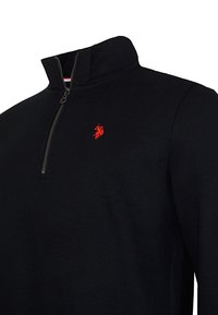 Czarny sweter z kołnierzem na ćwierć zamka, z małym czerwonym haftowanym logo na piersi. Wykonany z miękkiej, teksturowanej tkaniny.