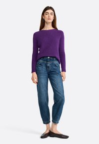 Purple, fluffy knit sweater with a wide neckline paired with blue, tapered jeans. Brown flat shoes complete the outfit.