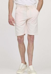 Shorts rose clair avec une taille élastique et un cordon de serrage, des poches latérales et une coupe décontractée, associés à des baskets blanches.