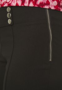 Black pants featuring three metallic buttons at the waist and a side zipper. Fabric appears stretchy with a smooth texture.