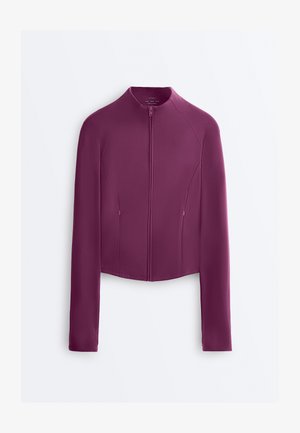 Pitkähihainen, vetoketjullinen takki syvän violetissa värissä, jossa korkea kaulus ja hienovaraiset saumasomisteet, aseteltu tasaisesti valkoista taustaa vasten.