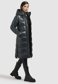 Tumši zaļš, spīdīgs pūkains mētelis ar kapuci, garā garumā un ar aizdari priekšpusē. Apvienots ar spīdīgām melnām kaujas zābakiem.