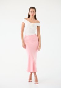Top bianco off-the-shoulder con dettaglio arricciato e fiore in tessuto; abbinato a una gonna rosa aderente. Tessuto liscio, silhouette elegante.