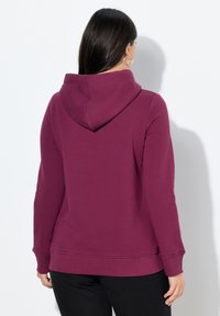 Felpa color mogano con un ampio cappuccio morbido, maniche lunghe, polsini a costine e orlo fitted. Design casual e comodo.