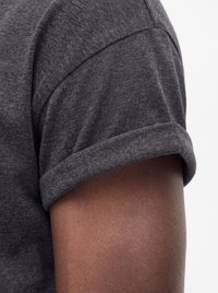 Close-up of a rolled short sleeve on a dark gray t-shirt worn on a bare arm with medium brown skin tone.