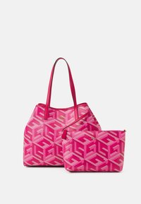 Twee roze Guess-tassen met een geometrisch logopatroon, een tote met schouderbanden en een met rits afsluitbare pouch, tentoongesteld op een witte achtergrond.