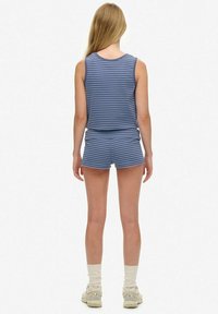 Completo estivo composto da canotta a righe blu e pantaloni corti. Tessuto morbido e leggero con una vestibilità aderente. Modello che indossa calzini beige e sneaker.
