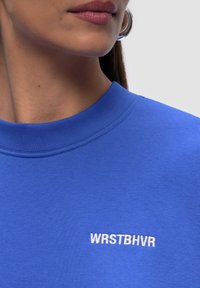 Felpa blu con scollatura rotonda, caratterizzata da testo ricamato bianco "WRSTBHV". Tessuto della superficie morbido e design aderente.