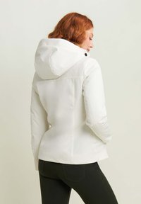 Giacca bianca con cappuccio dal design aderente e texture liscia, con bottoni neri decorativi sul cappuccio e una silhouette elegante.