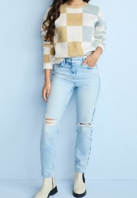 Kirjava vaalean beige neule, jossa on vaaleansinisiä ja sinapinkeltaisia ruutuja; yhdistetty vaaleansinisiin korkeavyötäröisiin farkkuihin, joissa on kuluneet polvet; vaaleanbeige nilkkurit.