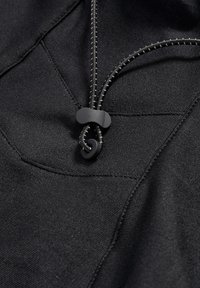 Zwarte stof met een gladde textuur, inclusief een trekkoordsluiting en toggles, evenals zichtbare stikseldetails en een geometrisch patroon.