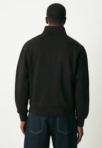 Black sweatshirt with a high collar and ribbed cuffs, made of soft fabric. The back features a clean design with no visible logos or patterns.