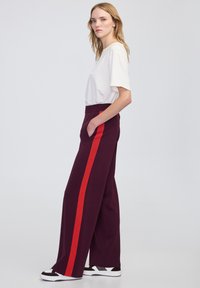 Szerokie, bordowe spodnie z czerwonymi bocznymi paskami, z talią o średnim podniesieniu i kieszeniami bocznymi, w połączeniu z gładką białą koszulką.