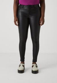 Black faux leather skinny pants with a smooth texture, high waist, and slight sheen, paired with cream-colored platform shoes.