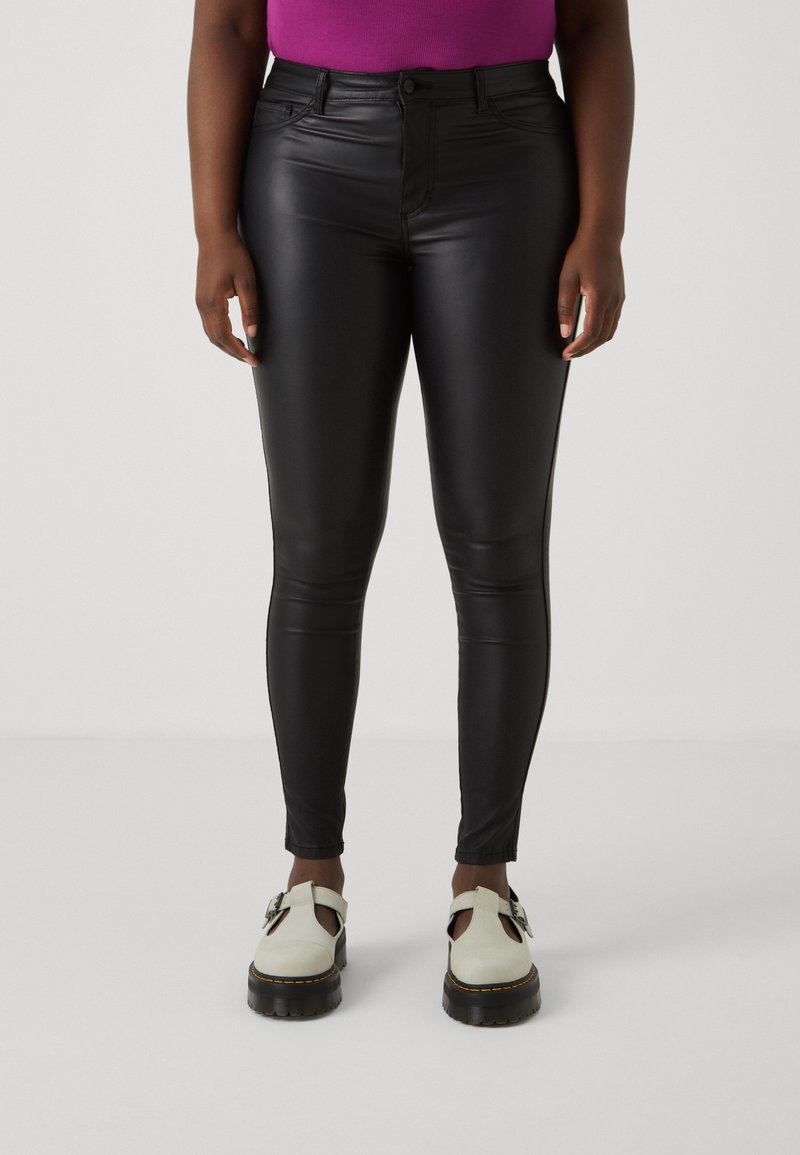 Black faux leather skinny pants with a smooth texture, high waist, and slight sheen, paired with cream-colored platform shoes.