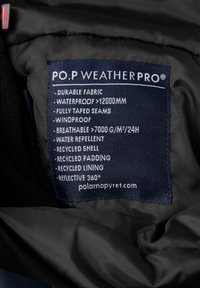 Blauwe label op een zwart kledingstuk met tekst die kenmerken beschrijft: waterdicht, ademend, winddicht, duurzaam materiaal en gerecyclede materialen.