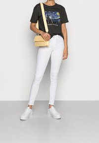 Sort t-shirt med et Van Gogh-graphic, hvide skinny jeans, hvide platform sneakers og en lille håndtaske i gul krokodillestruktur.