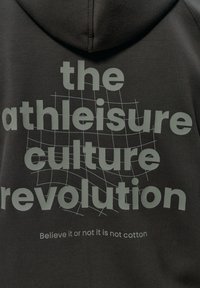 Čierna mikina s mäkkou textúrou, na ktorej je veľký šedý nápis: "revolúcia kultúry athleisure" a menší text nižšie: "Ver alebo nie, nie je to bavlna."
