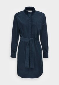 Laivaston sininen corduroykangasta valmistettu paitamekko, jossa on kaulus, pitkät hihat ja yhteensopiva vyö. Varustettu rintataskulla ja hieman kaarevalla helman muotoilulla.