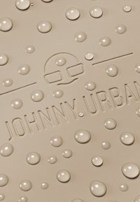 Beżowy materiał o fakturze z wypukłymi okrągłymi kroplami oraz tłoczonym logo "JOHNNY.URBAN", o minimalistycznym wzornictwie.