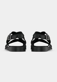 Czarne sandały z krzyżującymi się paskami i klamrą. Płaska podeszwa z niewielkim obcasem. Wykonane z tworzywa sztucznego o gładkiej fakturze.