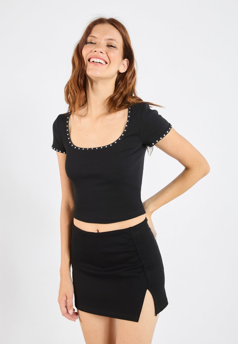 Svart ränderad crop-top med korta ärmar och fyrkantig halsringning, prydd med silvernitar längs halsringningen och ärmkanterna; matchas med en matchande minikjol.