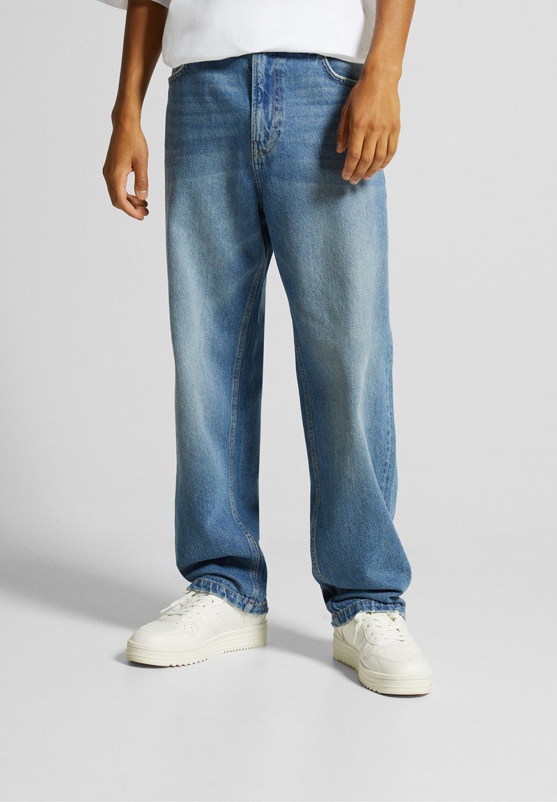 Ljusblå denimjeans med avslappnad passform, utrustade med fem fickor, dubbelsömmar och slitna detaljer. Matchas med vita sneakers.