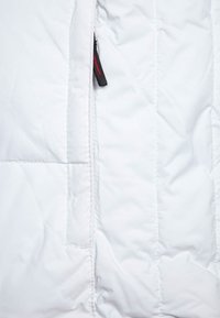 Vit isolerad jacka med quiltad textur. Har en siddragkedja med svart dragare och röd accent. Slät tygfinish.