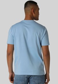 Svijetloplava pamučna majica s kratkim rukavima i okruglim izrezom, prikazana sa stražnje strane. Materijal izgleda mekano s glatkom teksturom.
