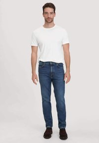 Witte T-shirt met korte mouwen, gecombineerd met mediumblauwe denim jeans en donkerbruine schoenen, met een klassieke pasvorm en eenvoudig ontwerp.