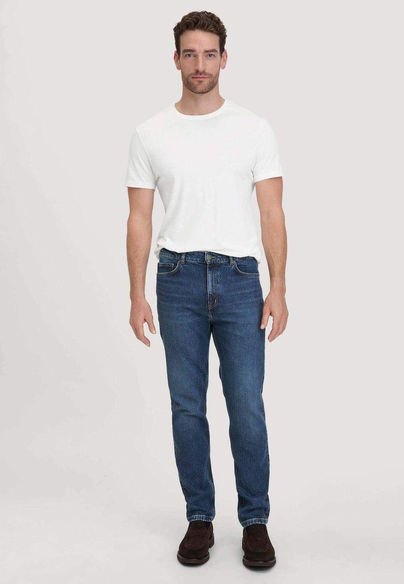 Witte T-shirt met korte mouwen, gecombineerd met mediumblauwe denim jeans en donkerbruine schoenen, met een klassieke pasvorm en eenvoudig ontwerp.