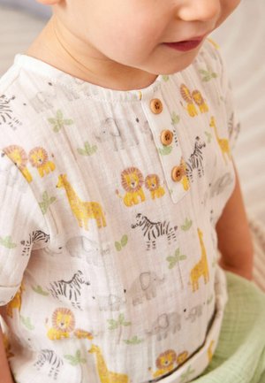 Småbarn iført hvid skjorte med træknapper og farverige dyreprint, herunder løver, giraffer, zebraer og elefanter.