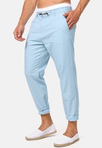 Pantaloni azzurri chiari, a gamba stretta, realizzati in cotone con risvolti, dotati di una vita con coulisse e tasche laterali. Design e texture casual.