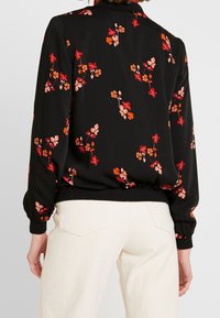 Blusa nera a maniche lunghe con un motivo floreale in tonalità di rosa e arancione, caratterizzata da un orlo arricciato e polsini elastici per una vestibilità comoda.