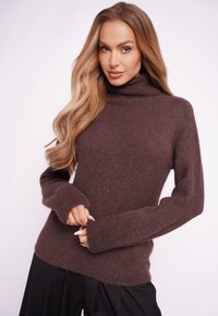 Brązowy golf wykonany z puszystego materiału, z długimi rękawami i luźnym krojem, w połączeniu z czarnymi, luźnymi spodniami.