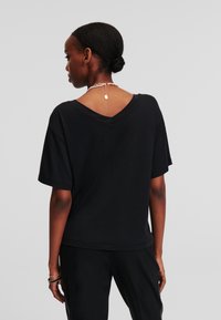 Tricou negru cu mânecă scurtă și decolteu în V. Textură netedă, croială liberă și design clasic. Fără motive sau logo-uri vizibile.