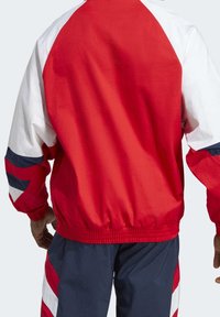 Cazadora corta roja y blanca con un corte holgado, que presenta mangas raglán, acentos en azul marino y puños y dobladillo elásticos. Material suave y ligero.