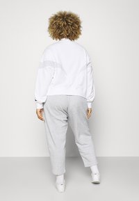 Sweatshirt branco com um corte descontraído e detalhes cinzas, combinado com calças de fato cinzentas claras. Textura em mistura de algodão, estilo casual.