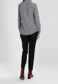 Svart- och vitrutigt skjorta med knappar och långa ärmar, tillsammans med svarta smalbyxor och bordeauxfärgade klackstövletter.