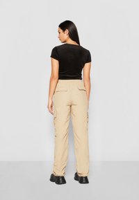 Svart kortärmad, figurnära t-shirt, kombinerad med beige cargobyxor med sidofickor och elastisk midja. Svarta skor fulländar looken.