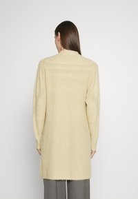 Cardigan lavorato a maglia in morbido beige, con un fit rilassato, maniche lunghe e un design di lunghezza intermedia, caratterizzato da un tessuto testurizzato e cuciture minime.