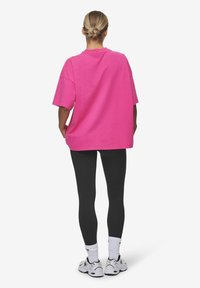 Överdimensionerad rosa t-shirt med korta ärmar, svarta leggings, vita sneakers med grå detaljer. Bakvy, mjukt bomullstyg, avslappnad passform.
