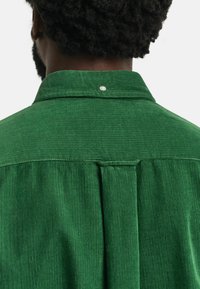 Chemise en velours côtelé vert avec un col structuré, un ribbing vertical distinct et une fermeture par un bouton à l'arrière.
