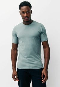 Gaiši zils īsroku T-krekls no mīksta kokvilnas ar apaļu kakla izgriezumu un pieguļošu dizainu, valkāts ar tumšām biksēm.