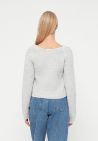 Szary, dziany sweter z szerokim dekoltem i długimi rękawami, zestawiony z niebieskimi dżinsami o wysokim stanie. Miękka tekstura i szczegóły w prążki.