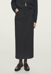 Donkergrijze, recht gesneden rok gemaakt van gestructureerde stof, met een zak op de taille, gecombineerd met bruine loafers en geribbelde sokken.