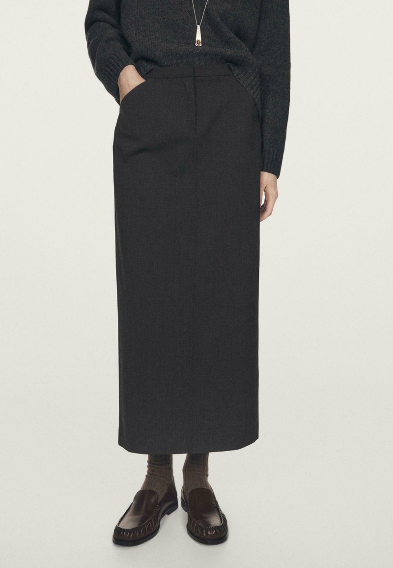 Donkergrijze, recht gesneden rok gemaakt van gestructureerde stof, met een zak op de taille, gecombineerd met bruine loafers en geribbelde sokken.