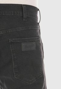 Jeans de mezclilla negra con un parche de cuero de la marca Wrangler en el bolsillo trasero, con costuras visibles y un diseño de cintura alta.